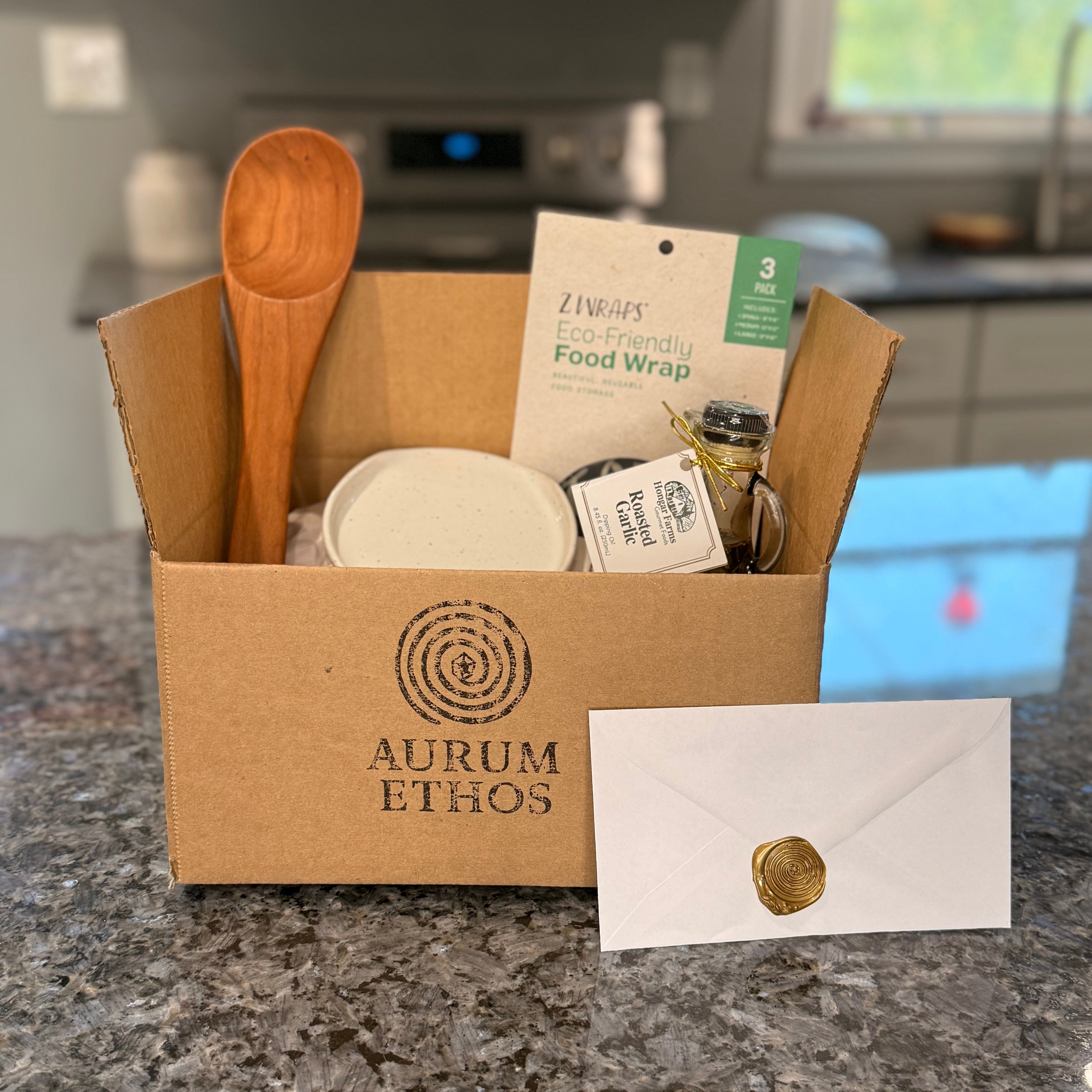 Kitchen Essentials Standard Story Box with a wooden spoon, eco friendly reusable food wraps, a bottle of roasted garlic olive oil, and a handmade ceramic spoon rest.