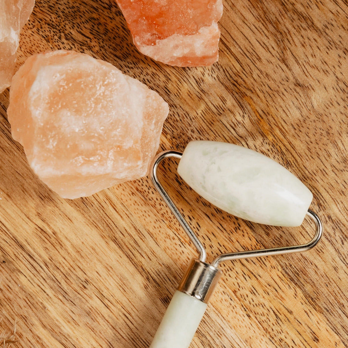 White jade roller on a wooden surface with Himalayan salt crystals